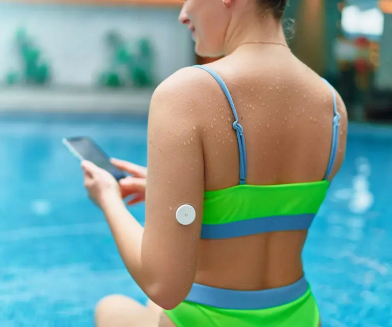 Active athletic fitness diabetic patient monitoring glucose level with remote sensor while training at swimming pool. Smart medical technology in diabetes treatment