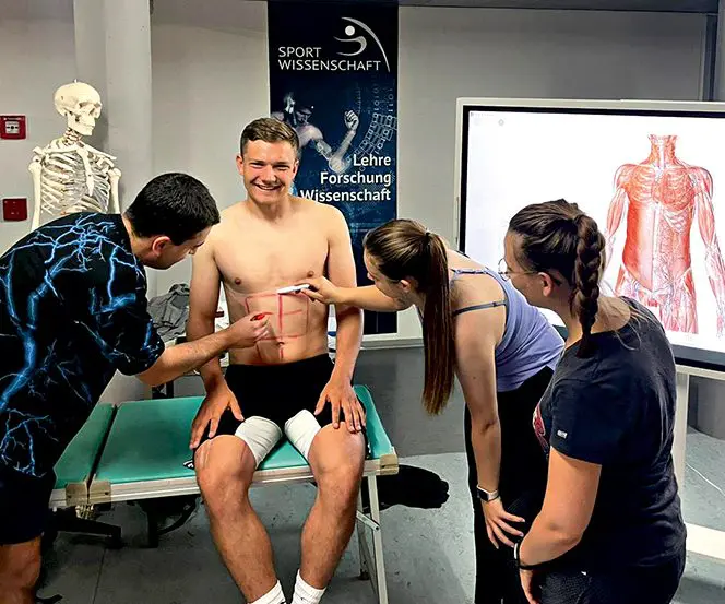 Oliver Ludwig zeigt Studierenden, wie man Muskeln bei einem Probanden ertastet.