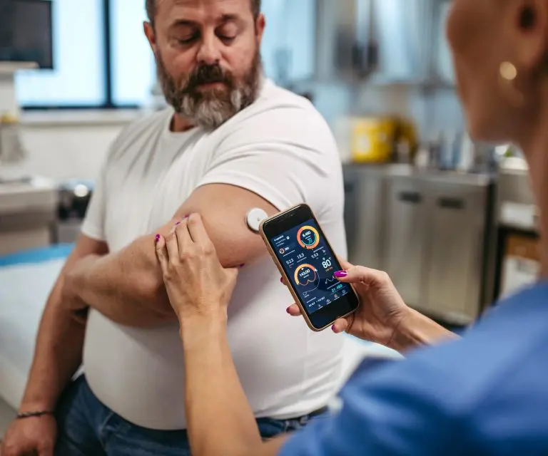 Krankenschwester misst Glukose bei einem Patienten mit CGM-System und Smartphone