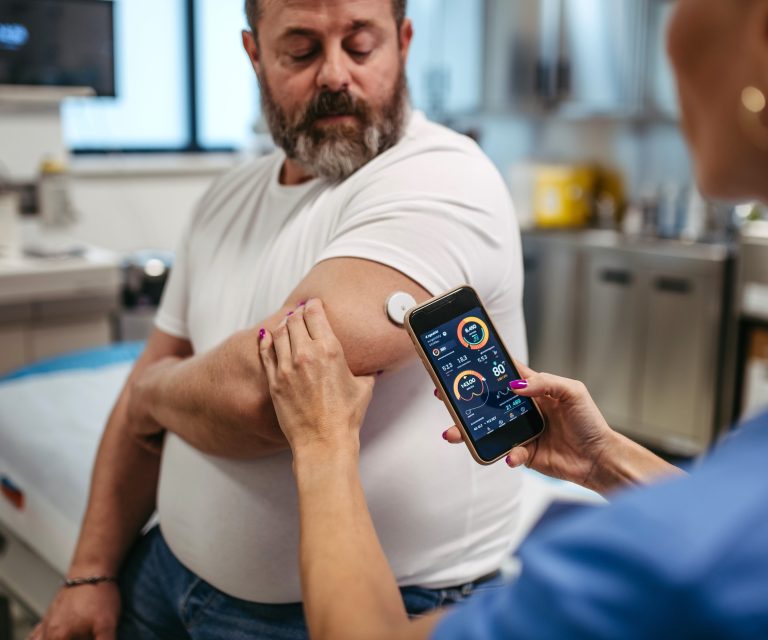 Krankenschwester misst Glukose bei einem Patienten mit CGM-System und Smartphone