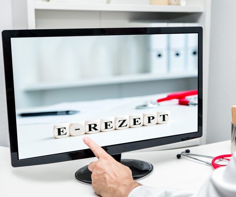 Arzt sitzt vor einem Monitor, der die Aufschrift E-Rezept zeigt