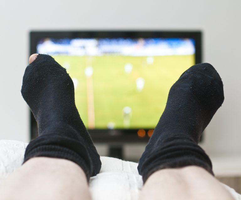 Übergewichtiger Mann auf dem Sofa schaut Fußballspiel im Fernsehen an.